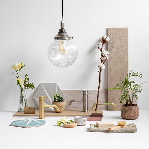 Laguna Bathroom Pendant light with ribbed glass globe shade hanging above a modern bathroom sink setup with gold and silver faucets and decorative plants