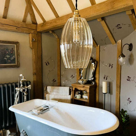 Camber large ribbed glass pendant light hanging above a freestanding bathtub in a rustic bathroom setting