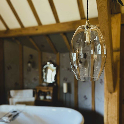 Camber large clear glass shade pendant light hanging in a rustic bathroom with wooden beams and a white bathtub