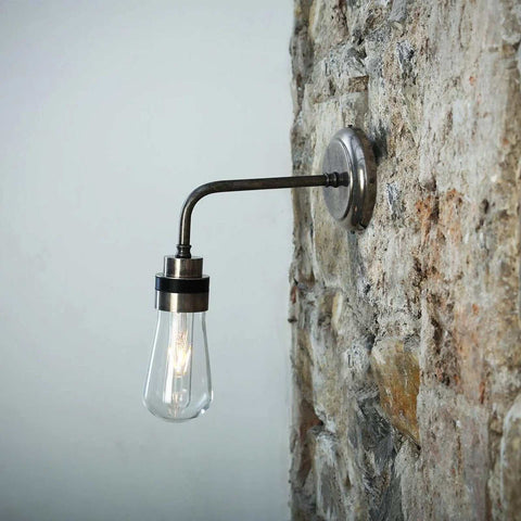 Bo Bathroom Wall light with industrial style, teardrop glass shade, and metal arm mounted on stone wall.