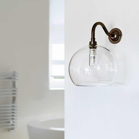 Soho medium clear glass shade bathroom wall light with curved swan neck and bronze finish mounted on white wall
