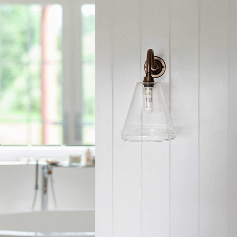 Rye small clear glass shade bathroom wall light with bronze fixture mounted on white wall near bathroom tub