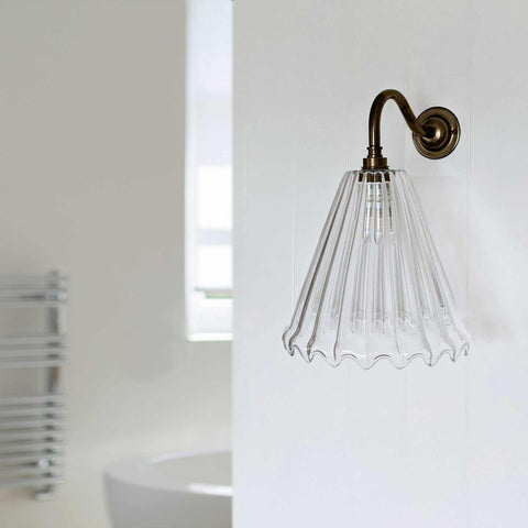 Rye medium ribbed glass shade bathroom wall light with bronze curved arm mounted on white wall above sink.