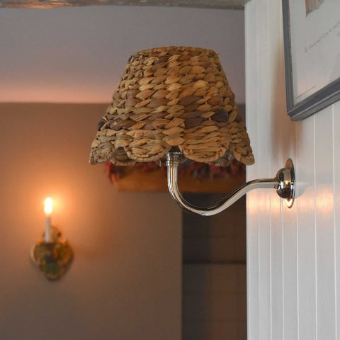Natural seagrass shade wall light with swan neck fitting in a cozy interior setting