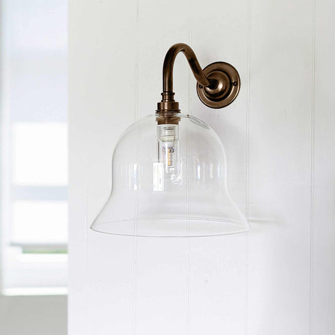 Clear glass wall light with bell-shaped shade, enhancing modern and traditional interiors, ideal for bathroom and home.