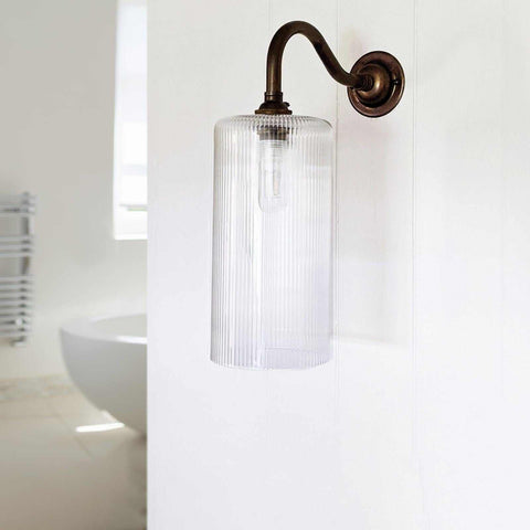 Brook Small ribbed glass shade bathroom wall light with bronze curved arm mounted on white wall in modern bathroom