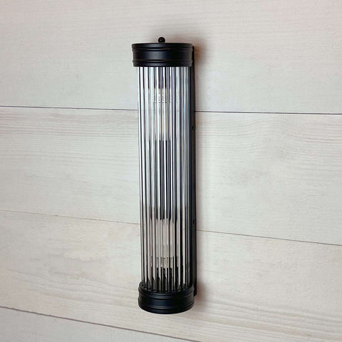 Modern black reeded bathroom wall light with glass rods and soft radiant glow for elegant mirror lighting