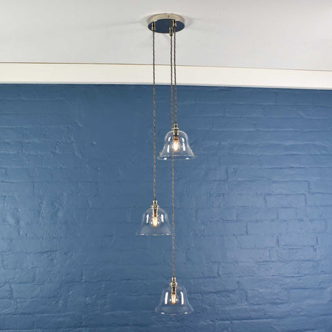 Bodium Medium Clear Glass Shade cluster pendant light with three hand-blown glass shades and adjustable cords against a blue brick wall