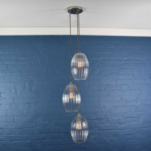 Camber Large Ribbed Glass cluster pendant light with three oval ribbed shades hanging against a blue brick wall