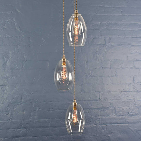 Camber Medium Clear Glass Shade cluster pendant light with three oval clear glass shades hanging against a blue brick wall background