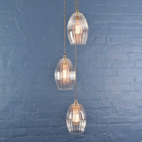 Camber Medium Ribbed Glass Shade cluster pendant light with three oval ribbed glass shades hanging against a blue brick wall