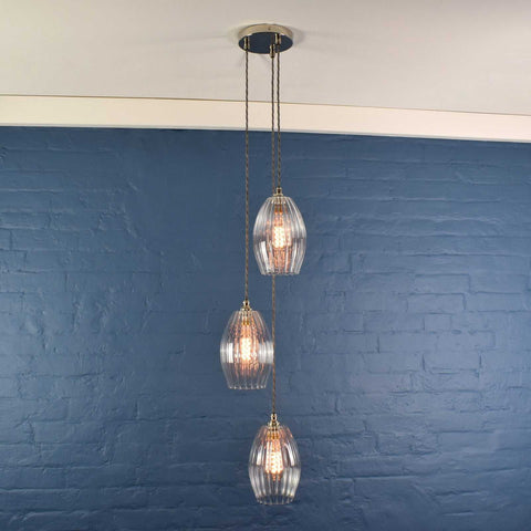 Camber Medium Ribbed Glass Shade cluster pendant light with three oval ribbed glass shades hanging at different heights against a blue brick wall background