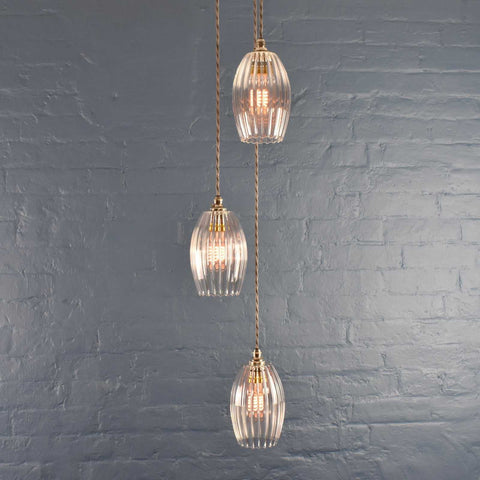 Camber small ribbed glass shade cluster pendant light with three hanging ribbed glass shades and twisted cords against a gray brick wall background
