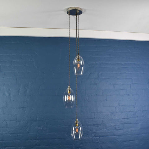 Camber small clear glass shade cluster pendant light with adjustable cords and hand-blown glass shades against blue brick wall