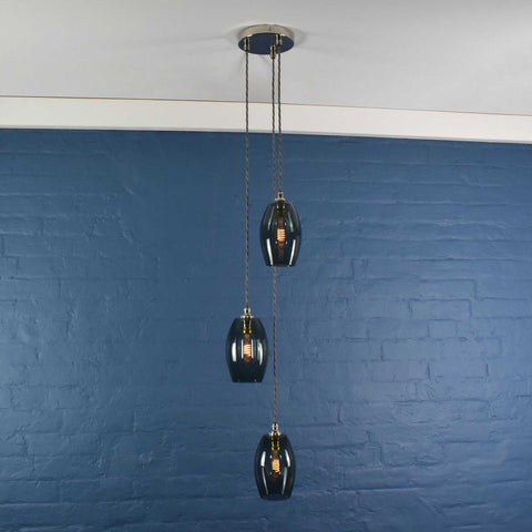 Camber small smoked glass shade cluster pendant light with three hanging smoked glass shades against a blue brick wall