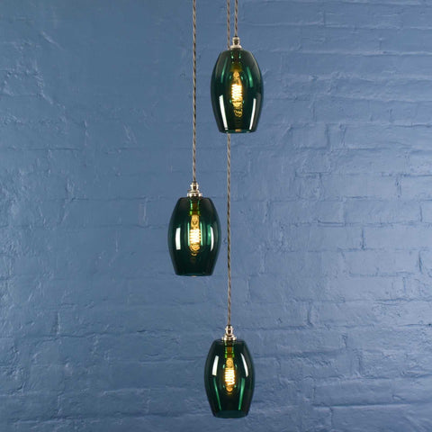 Camber Small Teal Glass Shade cluster pendant light with three hand-blown teal glass shades hanging against a blue brick wall