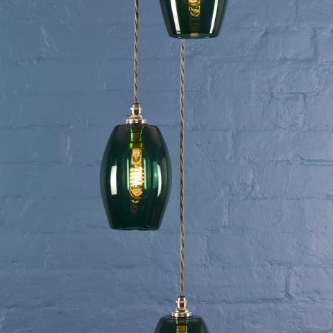 Camber small teal glass shade cluster pendant light with hand-blown glass and adjustable cord against blue brick wall