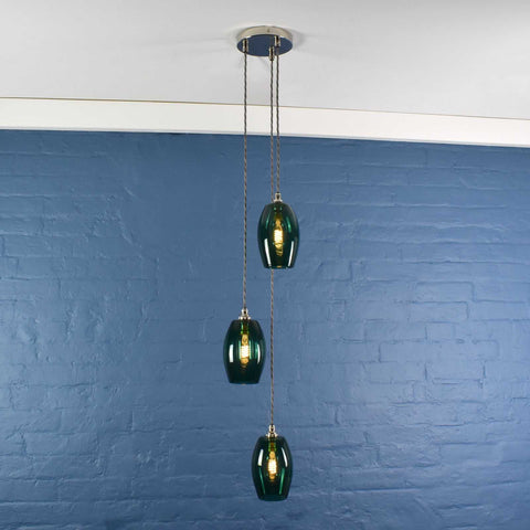 Camber small teal glass shade cluster pendant light with three hand-blown glass shades hanging against a blue brick wall background