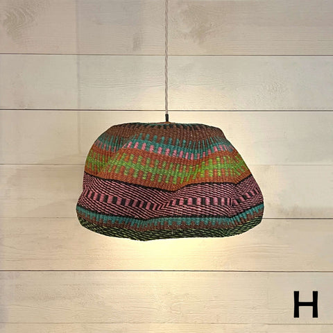 Woven colourful basket pendant light made from natural elephant grass hanging on a cord against a wooden wall background
