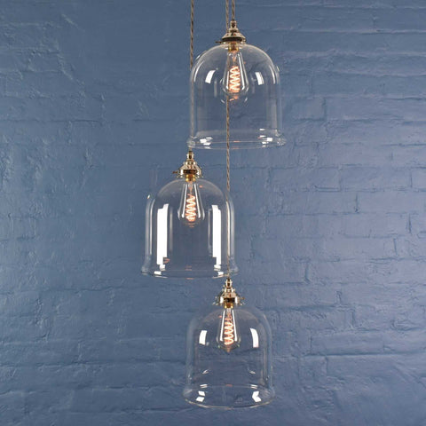 Hythe Medium Clear Glass Shade cluster pendant light with three hand-blown glass shades and vintage filament bulbs against a blue brick wall background