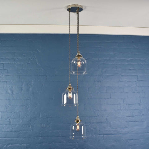 Hythe Small Clear Glass Shade cluster pendant light with three handblown bell-shaped glass shades hanging against a blue brick wall