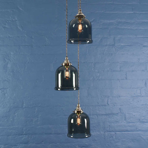 Hythe small smoked glass shade cluster pendant light with three hand-blown smoked glass cloche shades hanging against blue brick wall