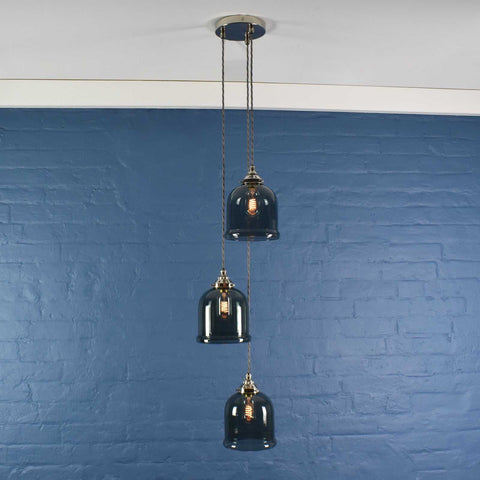 Hythe small smoked glass shade cluster pendant light with three hand-blown smoked glass cloche shades hanging against a blue brick wall