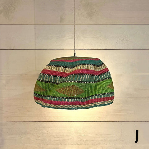 Woven colourful basket pendant light made from natural elephant grass with vibrant patterns hanging against a wooden wall background