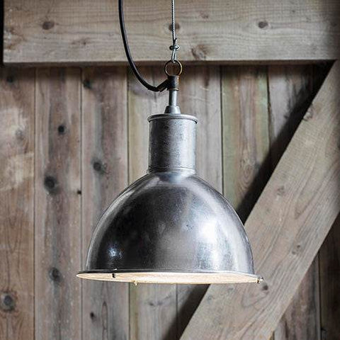 St Ives Bay Outdoor Pendant Light in galvanized steel with industrial dome design and brass connector hanging in rustic wooden setting