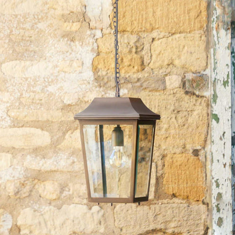 Pooky Crail Lantern outdoor ceiling light with brass frame and bevelled glass panels hanging against stone wall