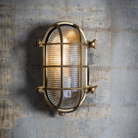 Devonport Bulkhead Wall Light vintage brass outdoor wall light with ribbed glass and protective cage mounted on textured concrete wall