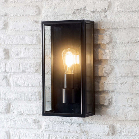 Belgrave Outdoor Lantern tall black wall light with clear glass and glowing bulb mounted on white brick wall