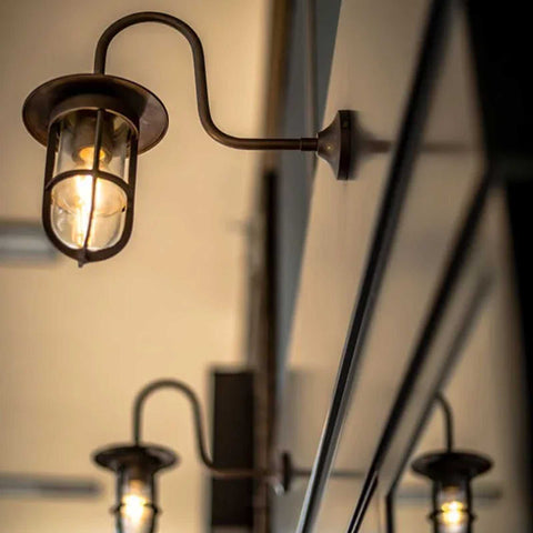 Denham Outdoor Swan Neck Wall Light with brass cage and glass shade, classic miner lamp style, warm outdoor lighting
