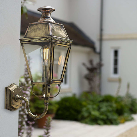 Chelsea Outdoor Wall Light in antique brass with copper detailing mounted on an exterior wall illuminating a garden pathway.