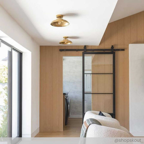 Telal Flush Ceiling Light in vintage brass finish installed in a modern hallway with wooden accent wall and sliding glass door.
