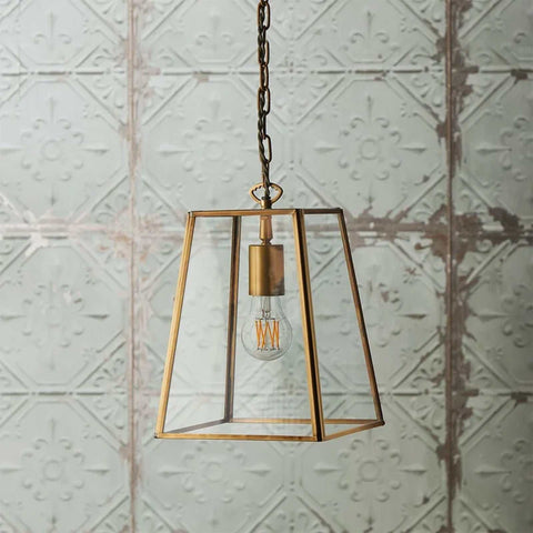 Medium Luxor Lantern Pendant Light with clear glass panels and antiqued brass frame hanging against textured wall