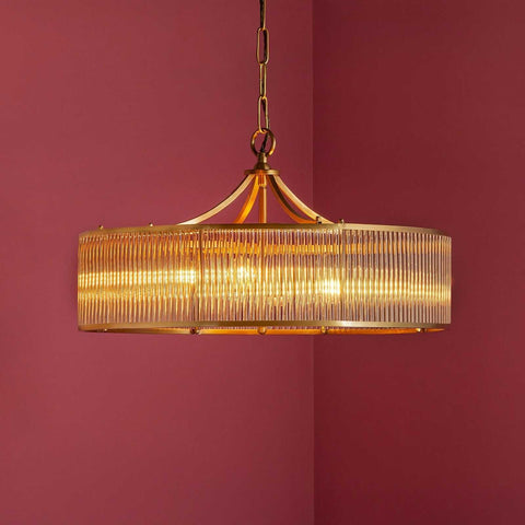 Pooky Athena Chandelier pendant light with brass frame and glass rods hanging against maroon wall