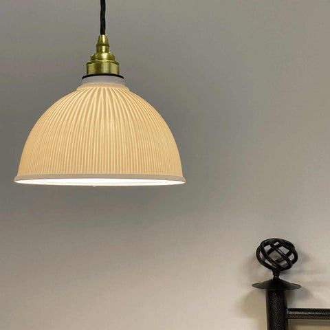 Denton Medium Ribbed ceramic pendant light with handcrafted ribbed porcelain shade and brass fitting hanging against a neutral wall.