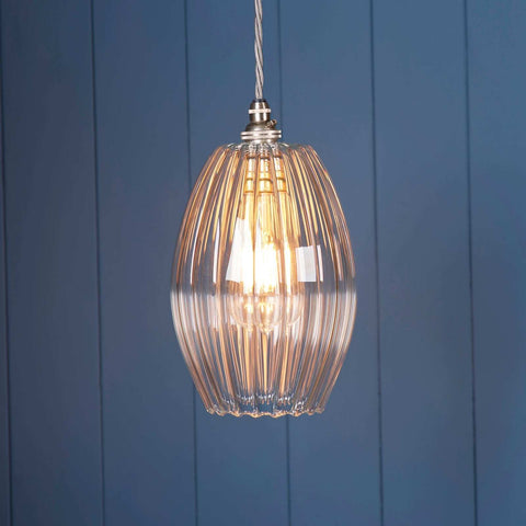 Camber Medium Ribbed Glass Shade pendant light with fluted glass design and warm illuminated bulb against blue panel wall background