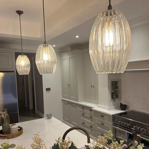 Camber large ribbed glass pendant lights hanging above a modern kitchen island with white countertops and grey cabinetry