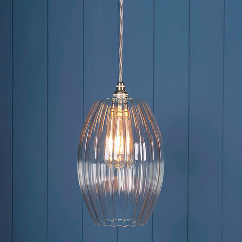 Camber Large Ribbed Glass pendant light with handcrafted ribbed shade and warm glowing bulb against blue panel wall background
