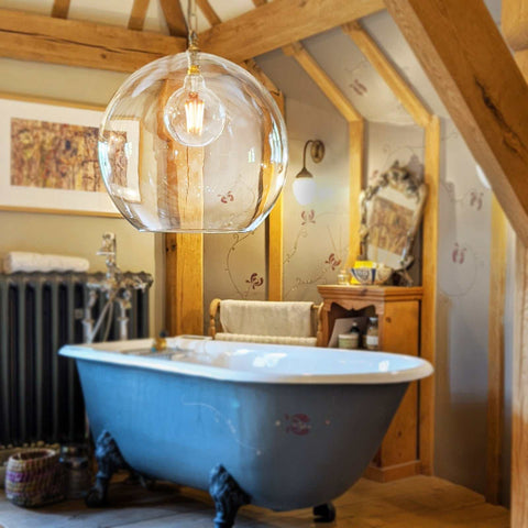 Soho XXL clear glass shade pendant light hanging above a vintage clawfoot bathtub in a rustic bathroom setting