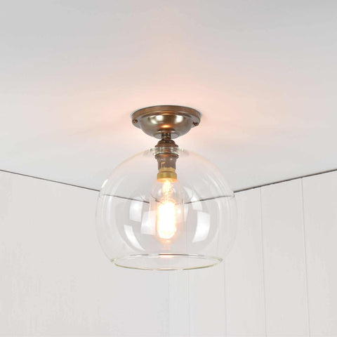 Soho medium clear glass globe flush ceiling light with antique brass finish and exposed bulb.