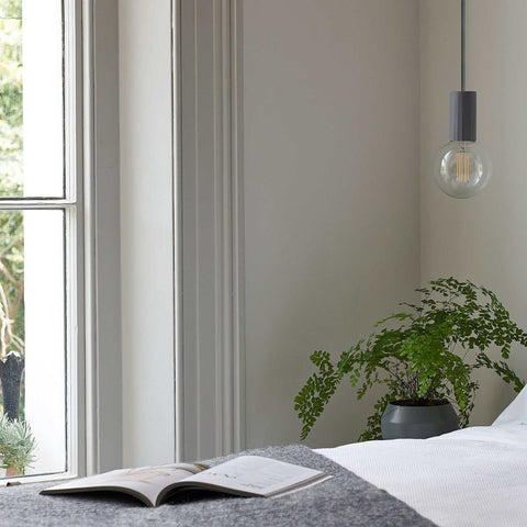 Modern Scandi Simple Bulb Pendant Light hanging beside a window in a minimalist room with a plant and an open book on a bed
