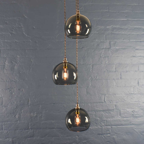 Soho Medium Smoked Glass 3 cluster pendant light with hand-blown smoked glass globes and twisted cords against a gray brick wall background