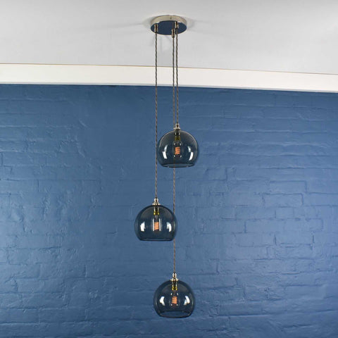 Soho Medium Smoked Glass 3 cluster pendant light with hand-blown smoked glass globes and adjustable cords against blue brick wall