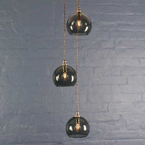 Soho small smoked glass shade cluster pendant light with three hand-blown globes and adjustable cords against a gray brick wall background