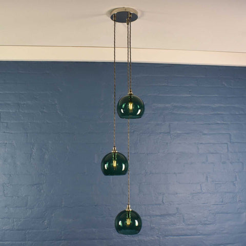 Soho small teal glass shade cluster pendant light with three hand-blown globes hanging against a blue brick wall