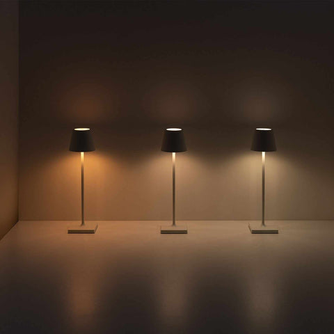 Three Zafferano Poldina Pro rechargeable sand table lamps emitting warm light in a minimal indoor setting