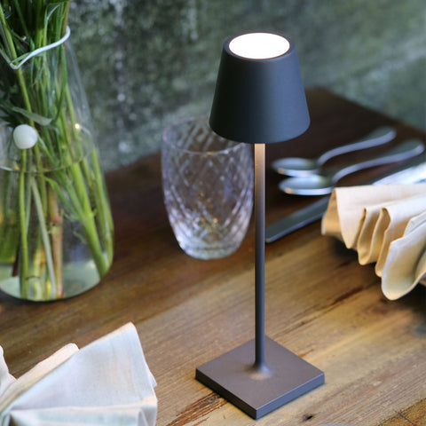 Zafferano Poldina Micro rechargeable black portable table lamp on wooden surface with glass and napkins nearby